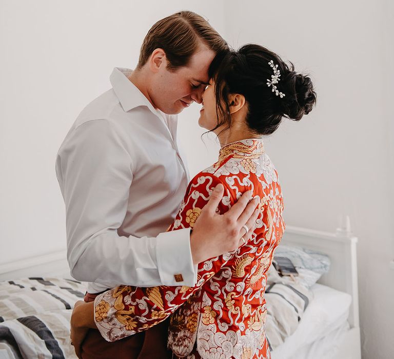 Bride in traditional red Chinese wedding dress embraces her groom before wedding ceremony 