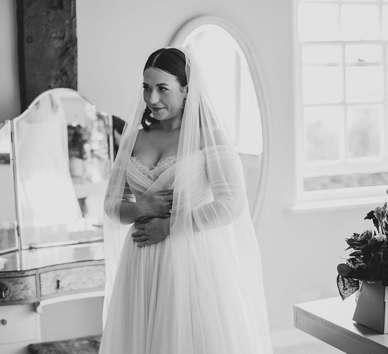 Bride in an off the shoulder long sleeve Wtoo by Watters wedding dress with a cathedral length veil getting ready for the wedding 