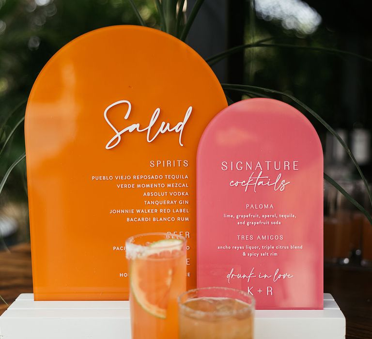 Pink and orange retro styled wedding signage beside cocktails 