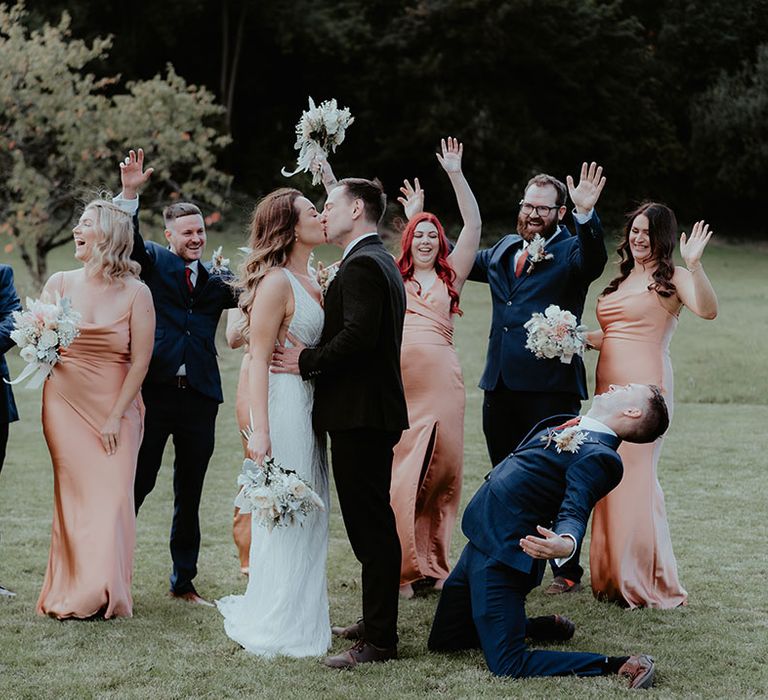 The bride and groom share a kiss as their bridesmaids and groomsmen celebrate and cheer for the kiss 