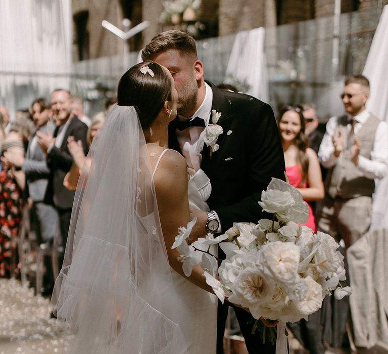 The bride holds her white wedding bouquet as the couple share a kiss after their ceremony 