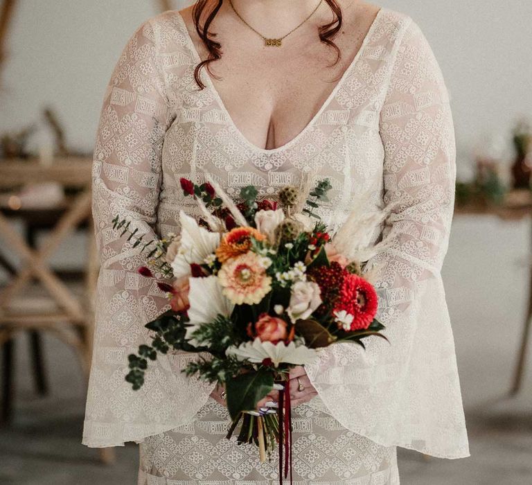 Bride in v-neck long bell sleeve boho wedding dress with boho rustic dried flower crown holding earthy toned garden rose, pampas grass, dried flower and foliage bridal bouquet in The Barn at Avington