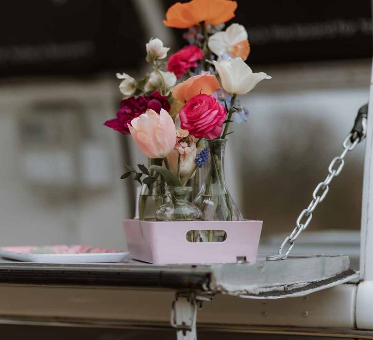 Spring coloured garden roses, peonies and carnations in small glass vases on wedding food truck 