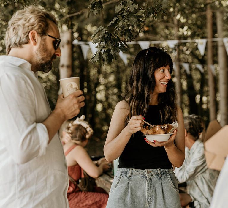 A wedding guest holds a recyclable cardboard box eating Mexican food served from food trucks 