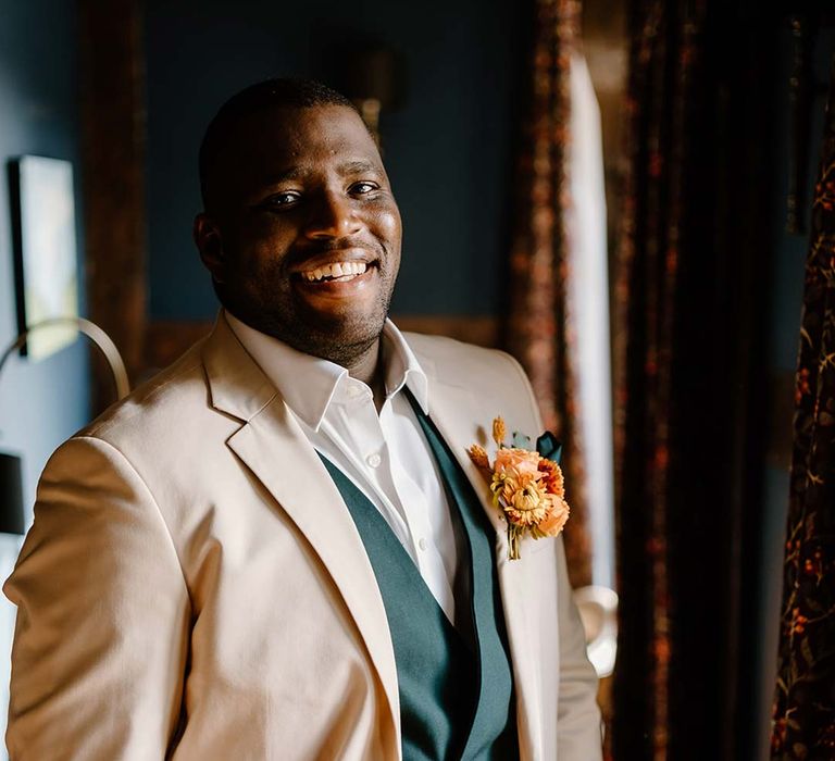 Groom in cream grooms morning suit with forest green grooms waistcoat and trousers, forest green pocket square and orange boutonniere 