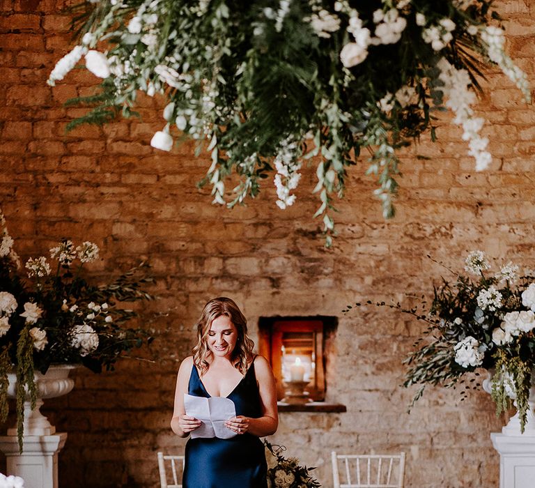 Bridesmaid in satin navy bridesmaid dress performing a wedding reading at the wedding ceremony 