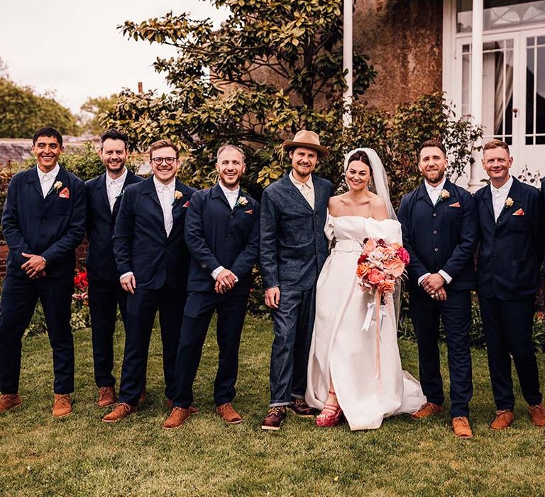 The groomsmen in navy suits posing with the bride and groom for large summer wedding 