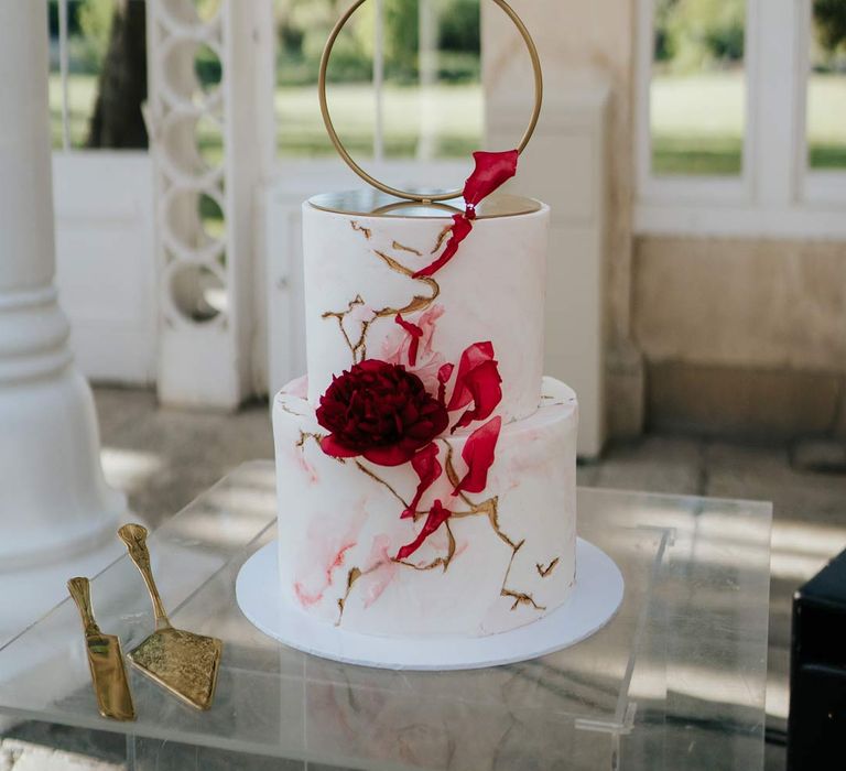 Artistic four tier wedding sculptural cake with hoop tier, gold icing, red icing and red rose decorations at Syon Park