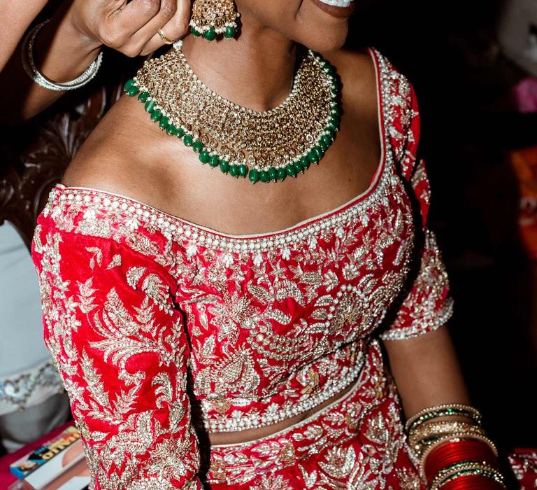 Bride in red and gold bridal lehenga and gold and green bridal jewellery 