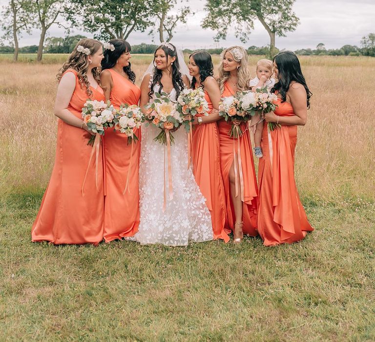 Bridesmaids in coral satin bridesmaid dresses with the bride for stunning bridal party photo 