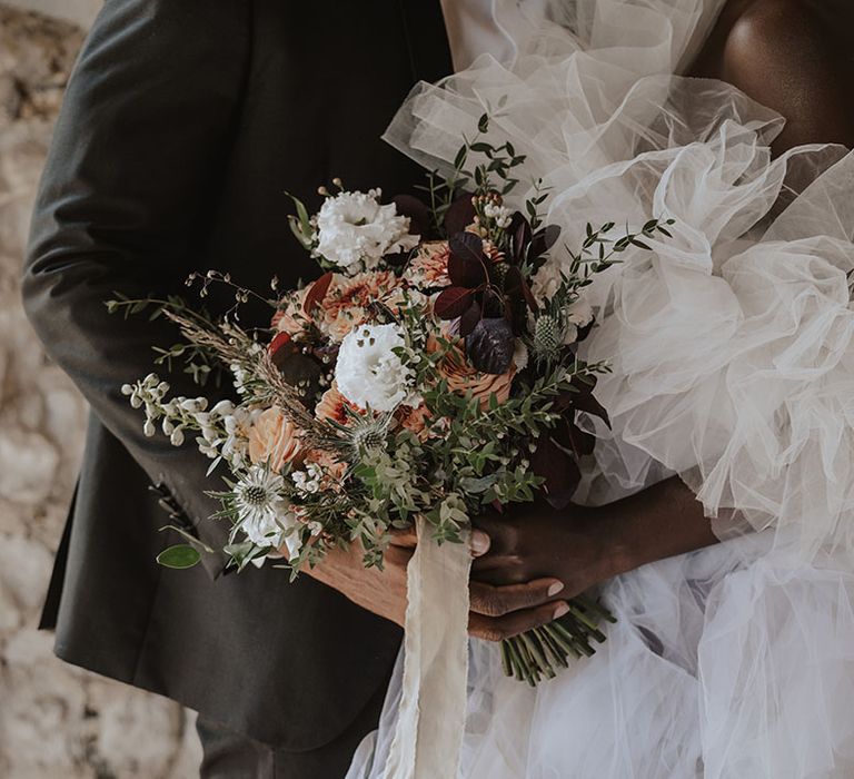 Bride in tulle wedding dress holding orange and white wedding bouquet 