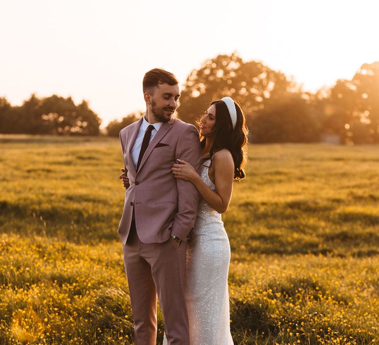 Golden hour wedding photo with bride embracing the groom in a dusky pink suit 