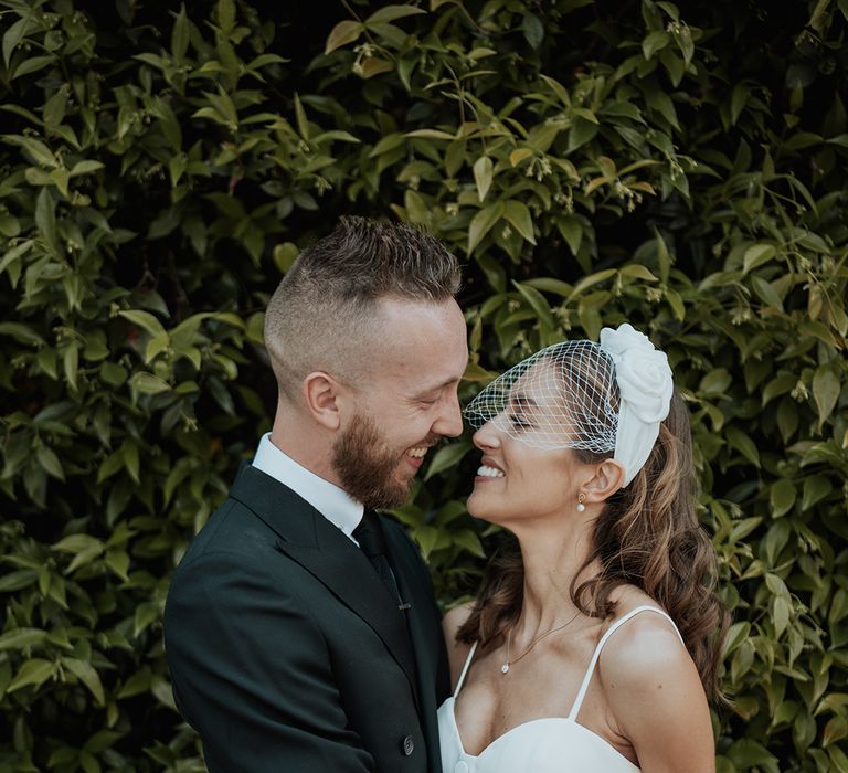 Groom in a black suit embracing his bride in a bridal top and skirt with birdcage veil at their stylish city wedding 