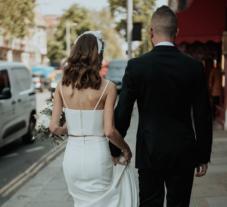 groom in a black suit holding the skirt train for his bride in bridal separates at urban wedding 