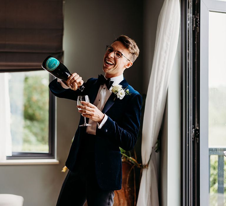 Luxe country house wedding with black tie dress code with groom in velvet tuxedo drinking champagne 