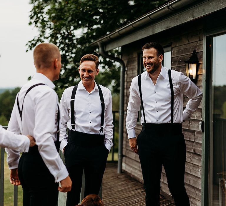 Groomsmen in shirts, black trousers and braces as they get ready for the wedding 