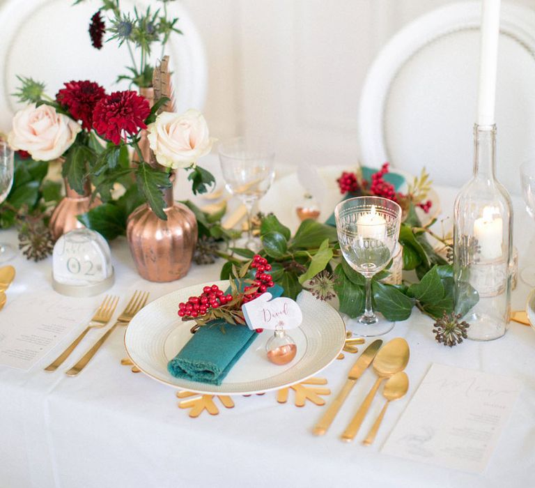 Christmas winter wedding table decor with red and green flowers and place setting including gold snowflake place mat and snow globe table number sign