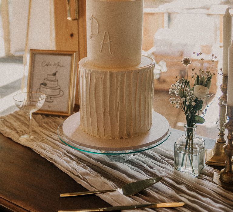 Three tier tall white iced wedding cake with the bride and groom's initials with pearls 