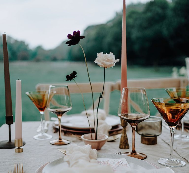 Simplistic wedding tablescape with neutral wedding flower arrangement, coloured glassware, and taper candles 