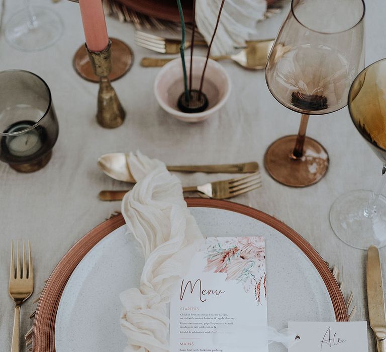 Wedding place setting with wicker place mat, wedding menu and white napkin with gold cutlery 