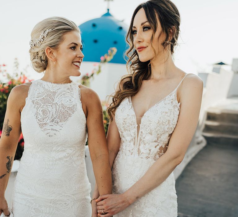 Brides in lace wedding gowns holding hands as they stroll around the stunning Santorini on their wedding day