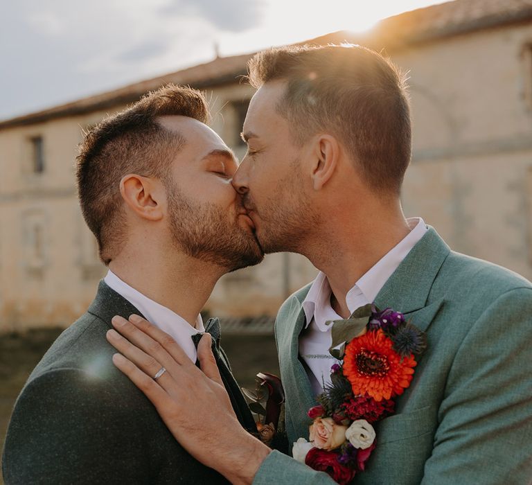 Two grooms sharing a kiss during golden hour at French wedding 