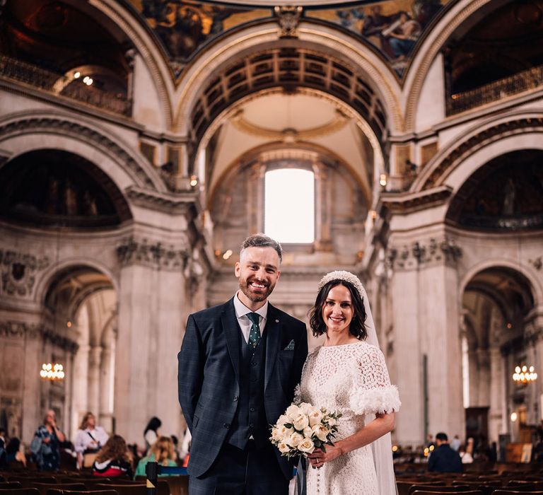 Groom in navy three piece wedding suit with the bride wearing a flower pattern wedding dress at St. Paul's cathedral 