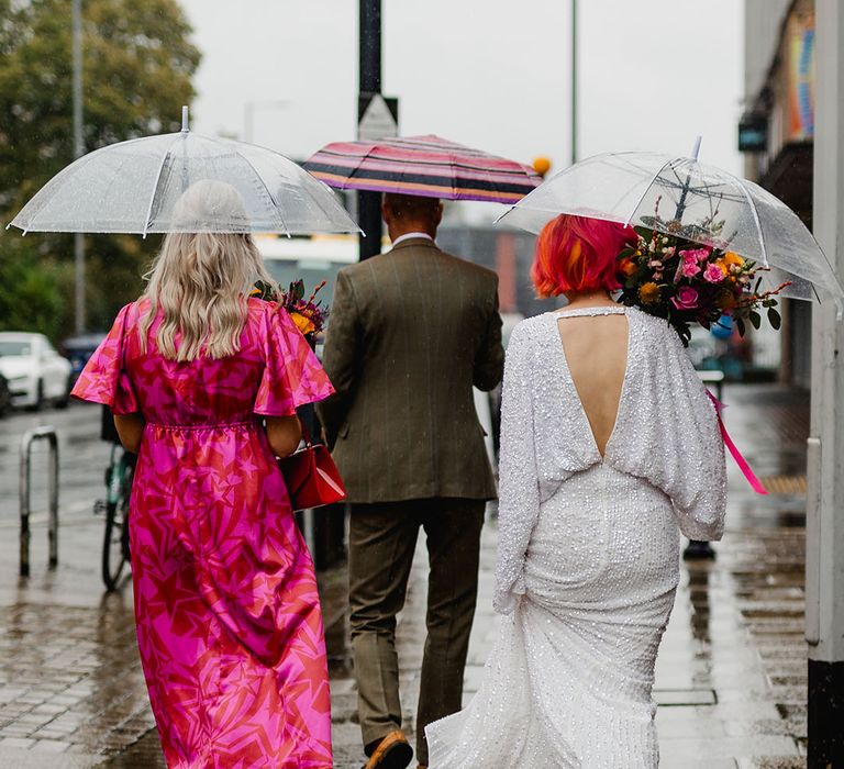 Bride wearing bat wing sequin wedding dress with umbrellas on rainy wedding day 