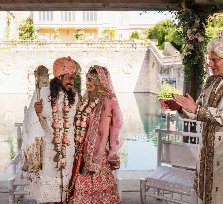 Bride and groom in pink, white and gold Indian wedding outfits at Hindu wedding ceremony 