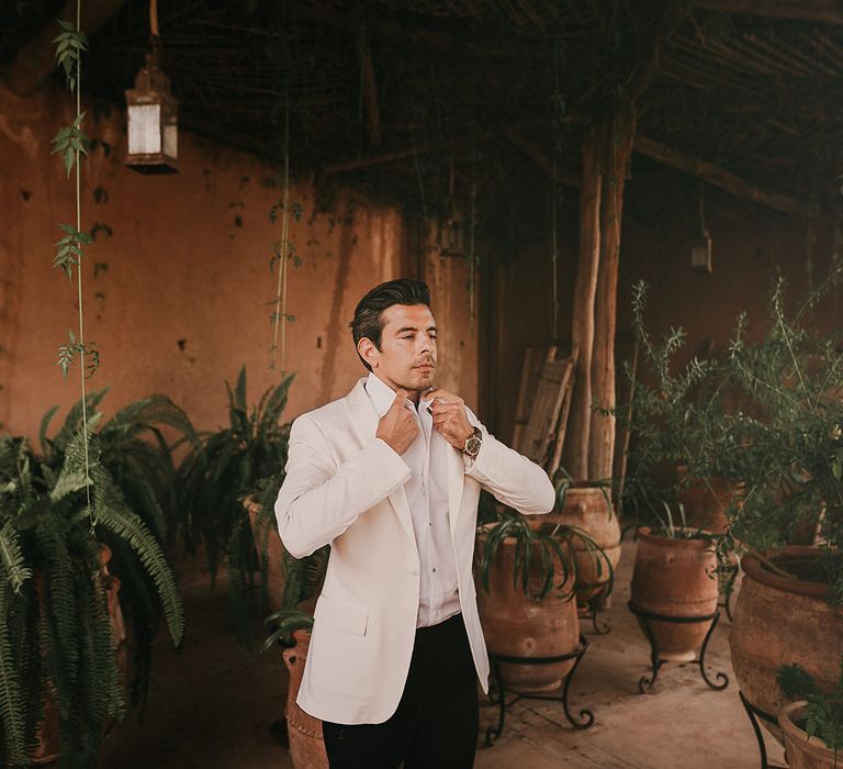 Groom on wedding morning getting ready in a white dinner jacket 