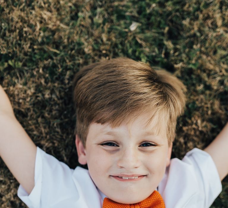 Young ring bearer in white shirt and bright orange bow tie to match the groom