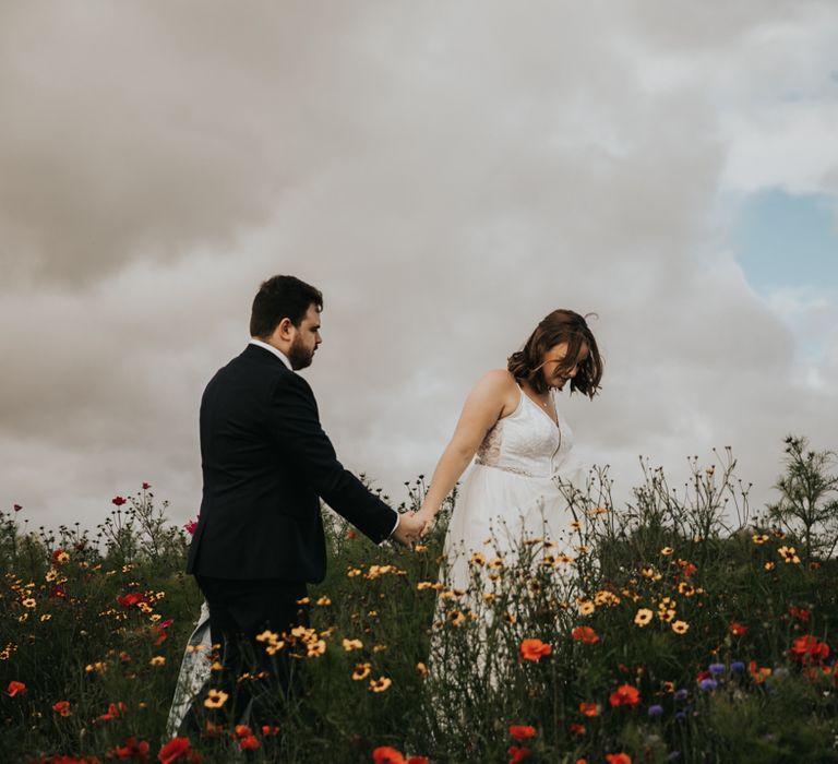 Bride and groom holding hands walking through wildflower meadow