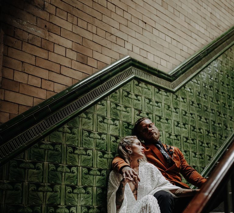 Bride and groom pose on stairs against green Victorian tiles