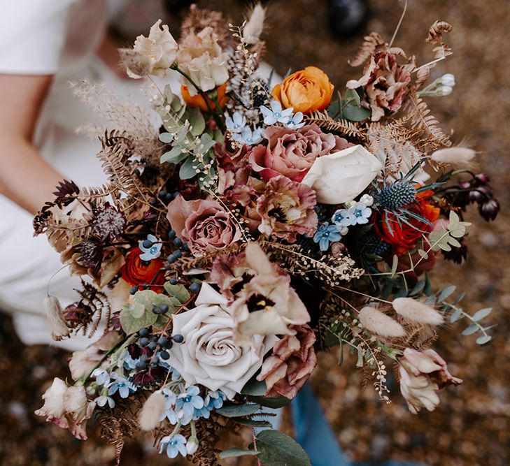 Close up of winter wedding bouquet with roses and dried flowers. There are small blue flowers and berries.