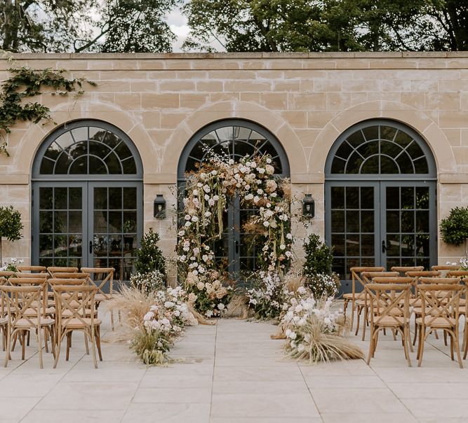 Outdoor ceremony at The Fig House, Middleton Lodge with floral arch altar decor and wooden chairs