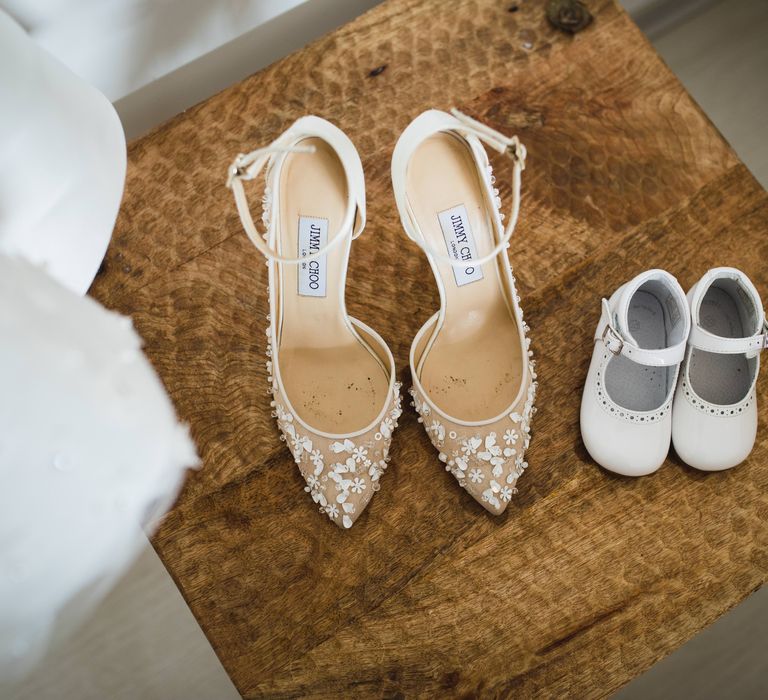 White floral Jimmy Choo wedding heels next to a small white pair of baby shoes