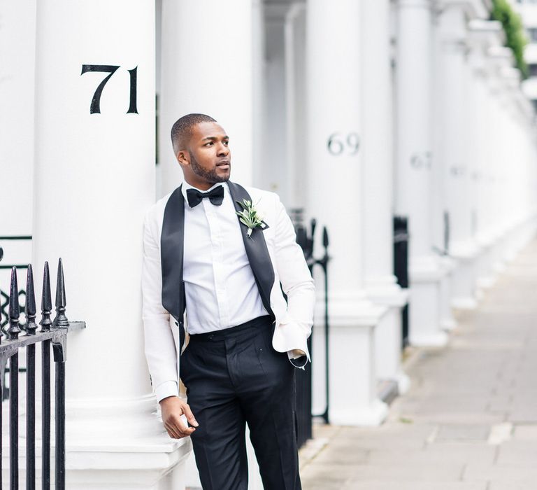 Groom leans into white pillar in London 