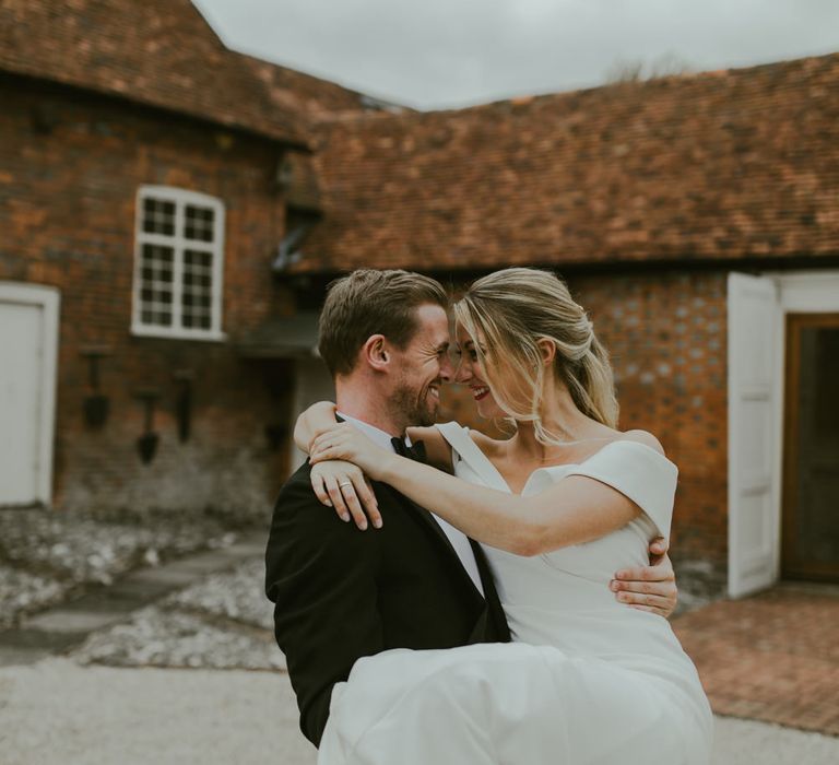 Groom holds bride as they lovingly touch heads outdoors