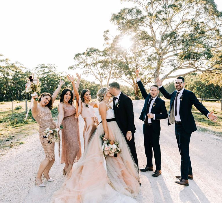 Bride in tulle skirt wedding dress kisses husband surrounded by bridesmaids and groomsmen