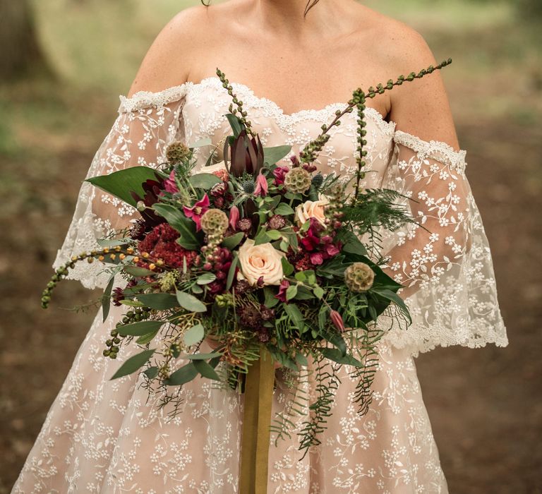 Bride stands wearing bridal gown and holds floral bouquet with pink blooms