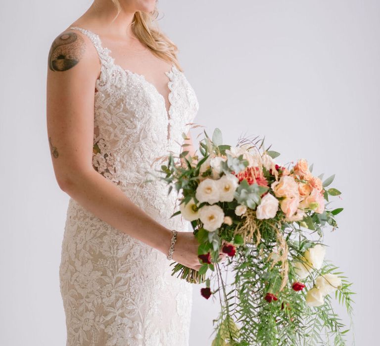 Bride wearing a lace mermaid wedding dress and diamond head piece, holding a bouquet of blush and terracotta flowers