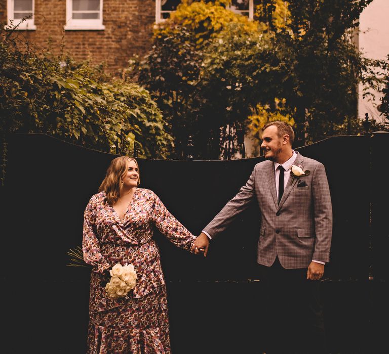 Bride & groom hold hands as they wear casual wedding outfits on the day of their wedding