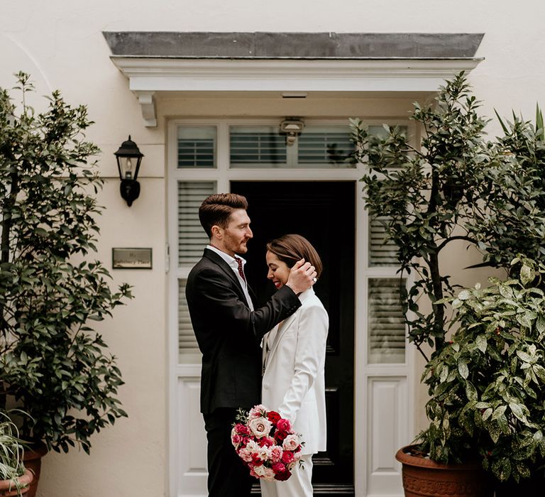 Groom tucks hair behind brides ear as they stand outdoors on their wedding day