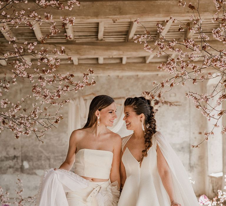 Two stylish brides in a mini wedding dress and bridal cape and trouser separates and detachable ruffle skirt 