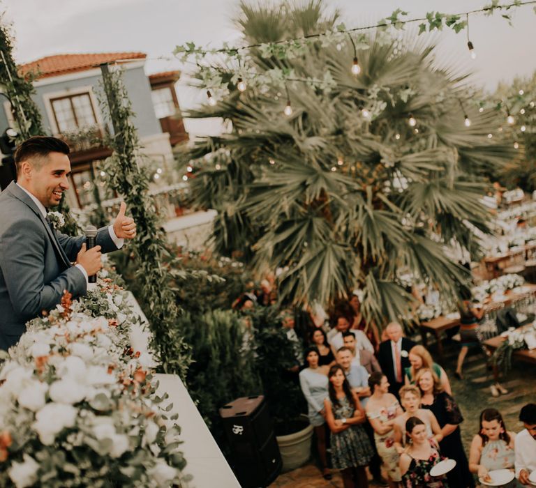 The groom looking out over a mezzanine at his guests, giving them a thumbs up