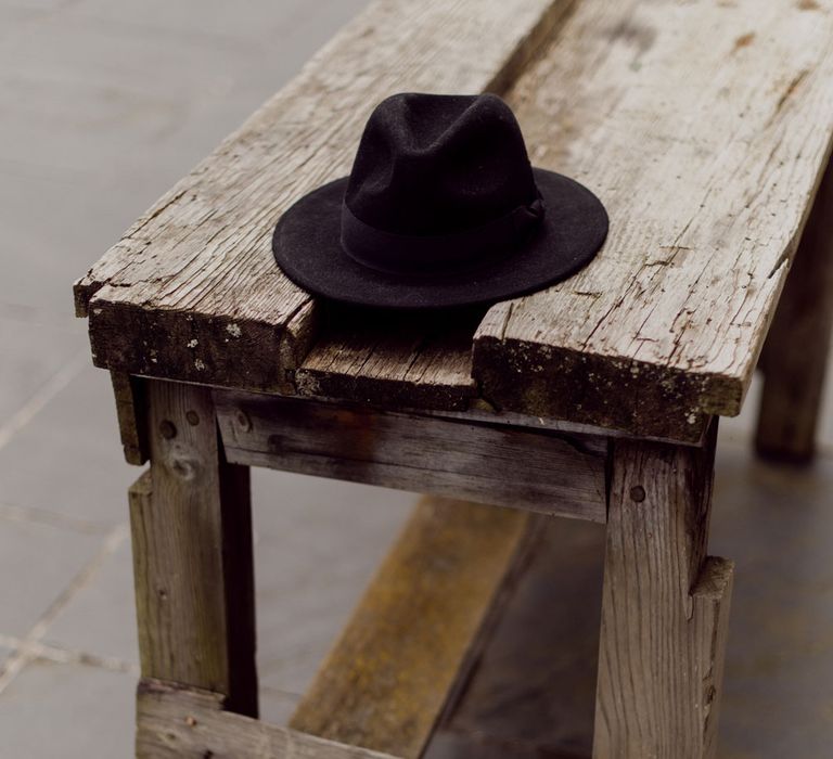 Black fedora hat on rustic wooden bench at garden party wedding in Devon with applique veil