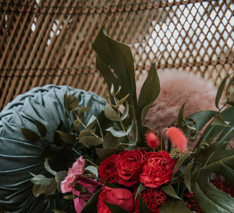 Red, pink and green wedding bouquet with roses and palm leaves laid on pink fluffy throw at festival themed wedding