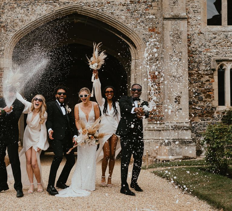 Fun wedding party portrait at modern luxury wedding with groomsmen popping and spraying champagne 