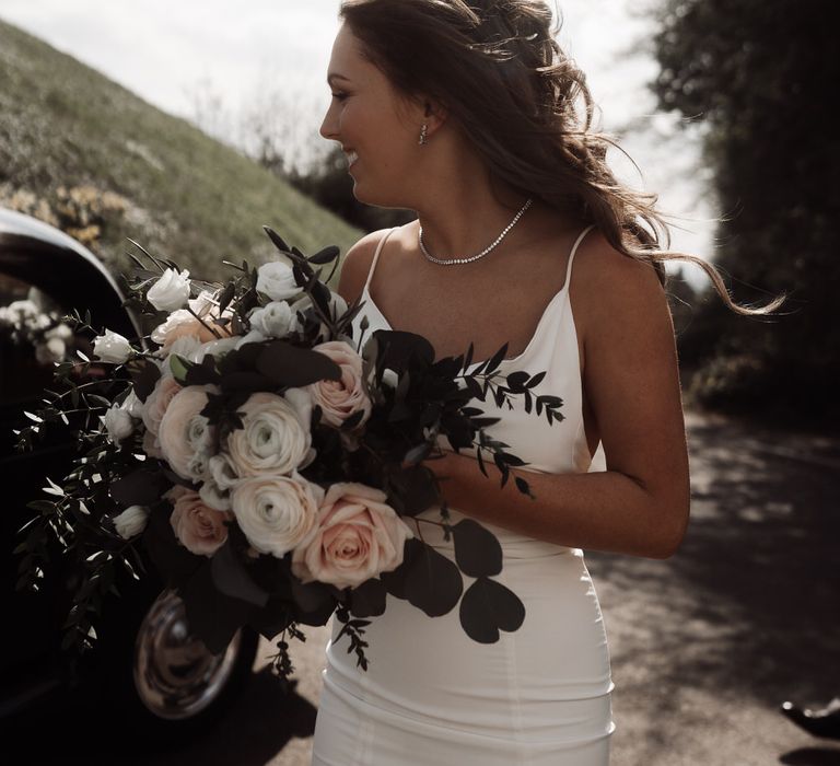 Bride wearing a white slip wedding dress holding a bouquet of white and pink roses