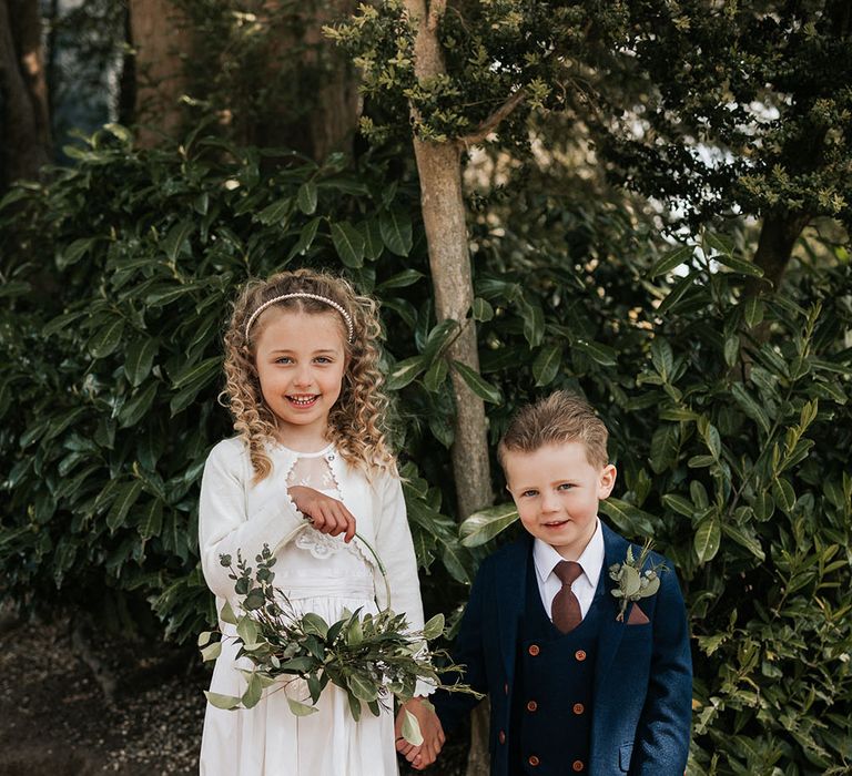 Flower girl and page boy in a white dress with flower basket and navy three-piece suit 